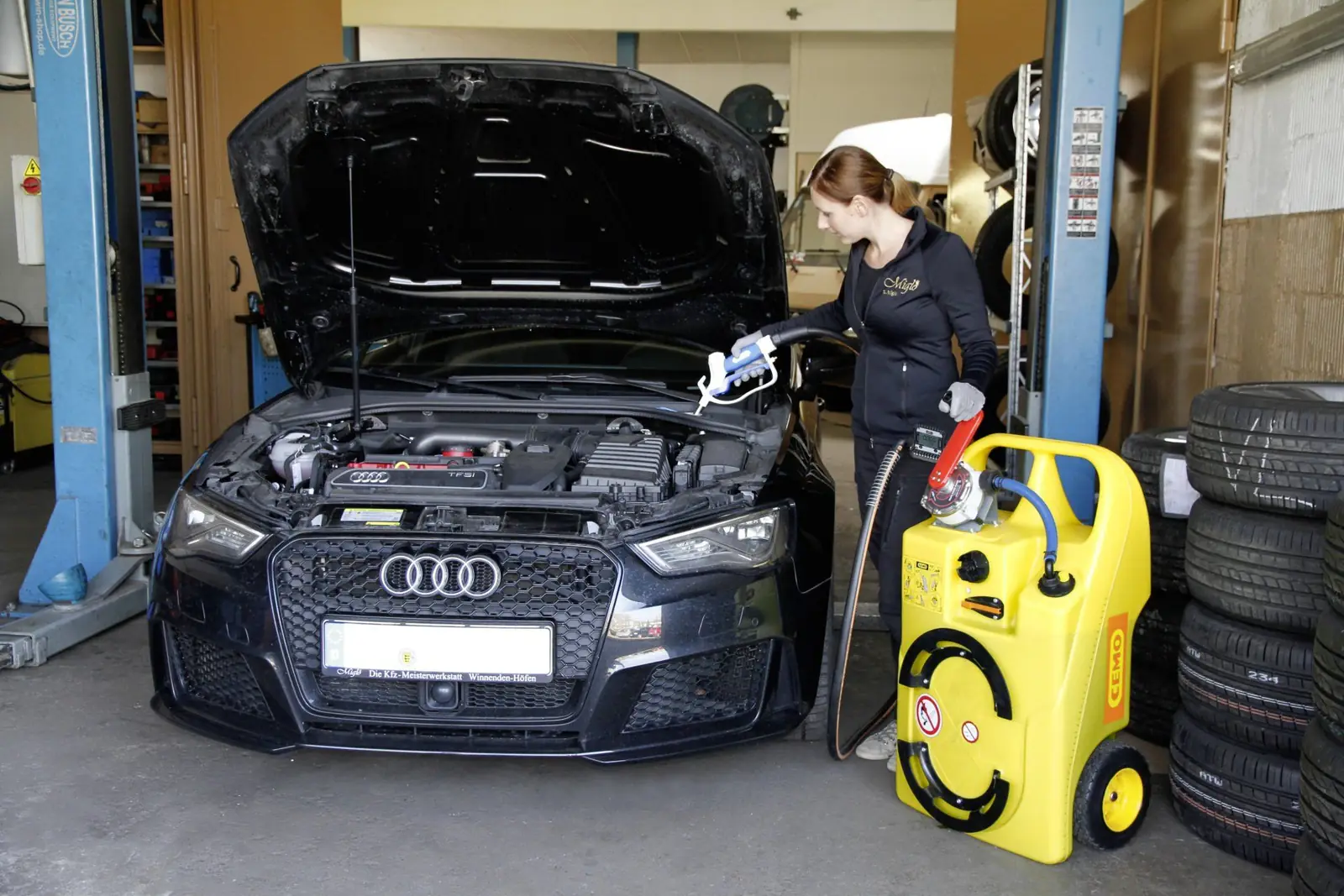 Mitarbeiterin der Kfz-Werkstatt Miglo füllt Scheibenwischwasser in einem Audi mit geöffneter Motorhaube nach